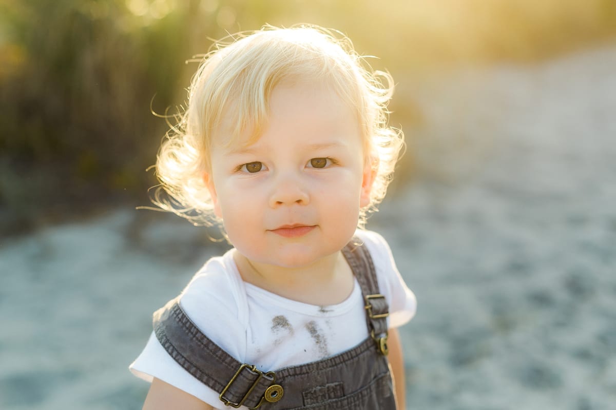 Portrait of a blond toddler boy in overalls on the beach