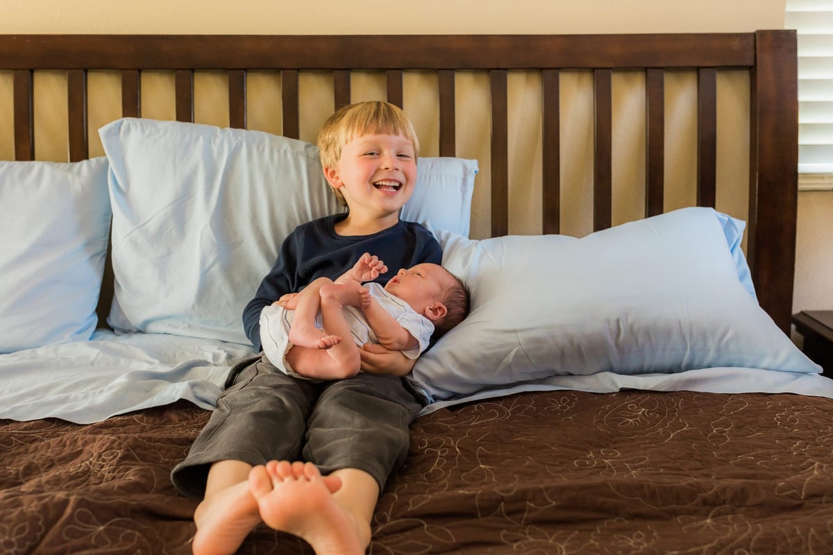 Laughing big brother holding his newborn sibling on the bed
