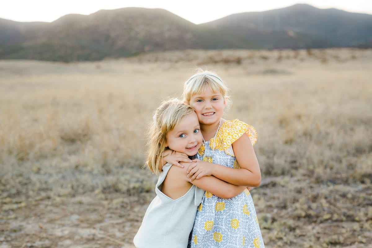 Two sisters hugging in a golden field below the mountains