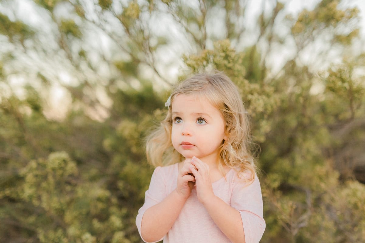 Toddler girl with clasped hands looking up in a green field