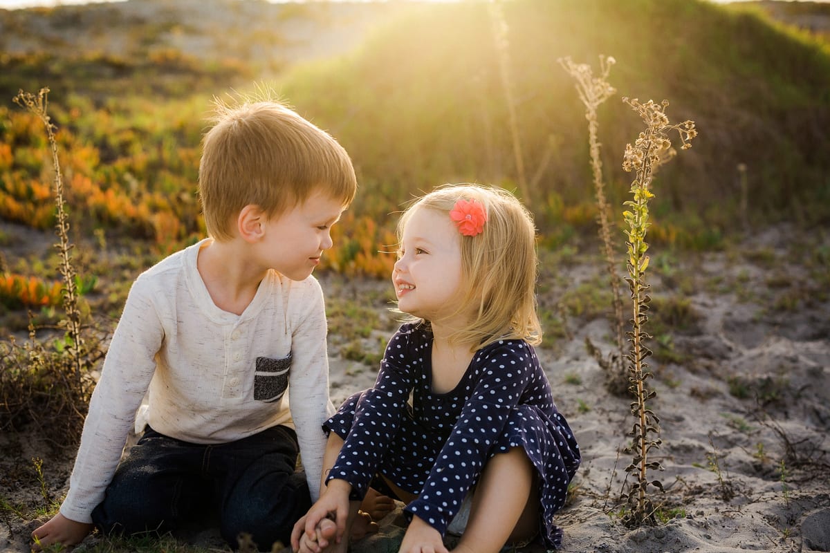 Brother and sister sitting in the sand dunes smiling at each other