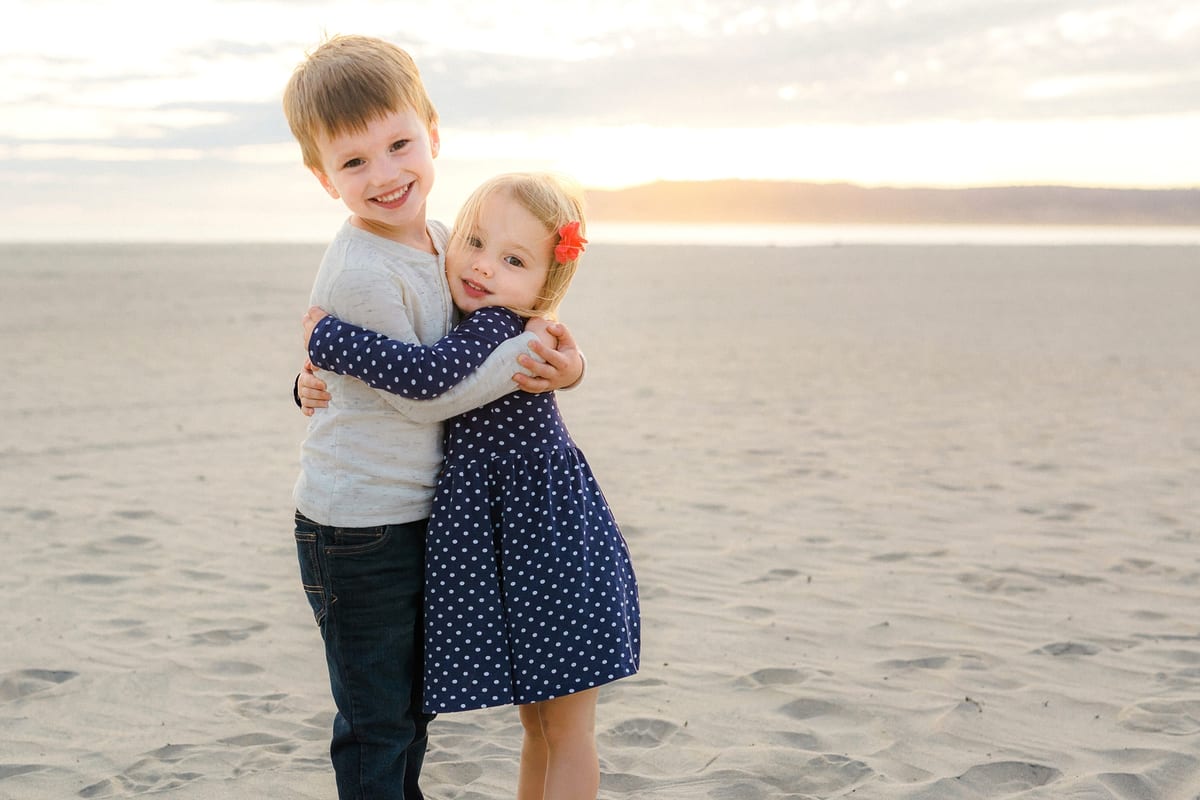 Brother and sister hugging on the beach at sunset