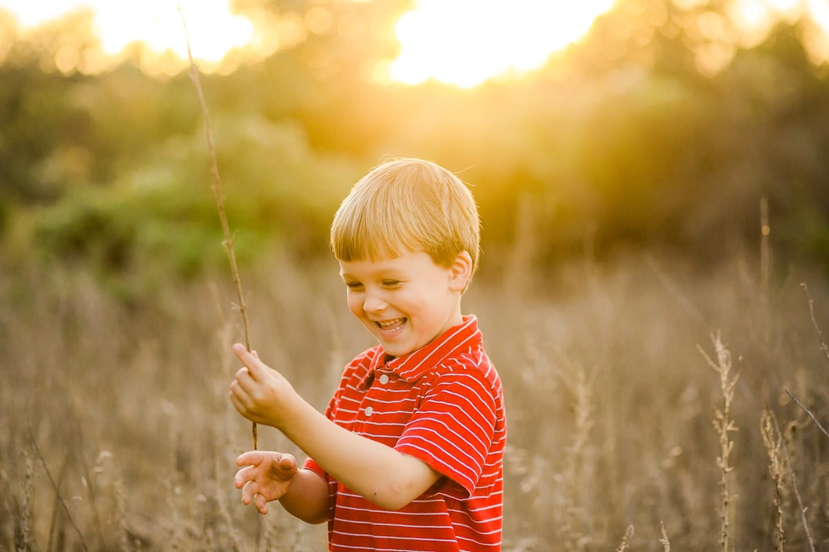 Smiling boy in a red shirt holding a stick in golden grass