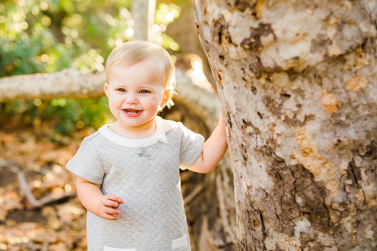 Smiling toddler girl standing beside a sycamore tree