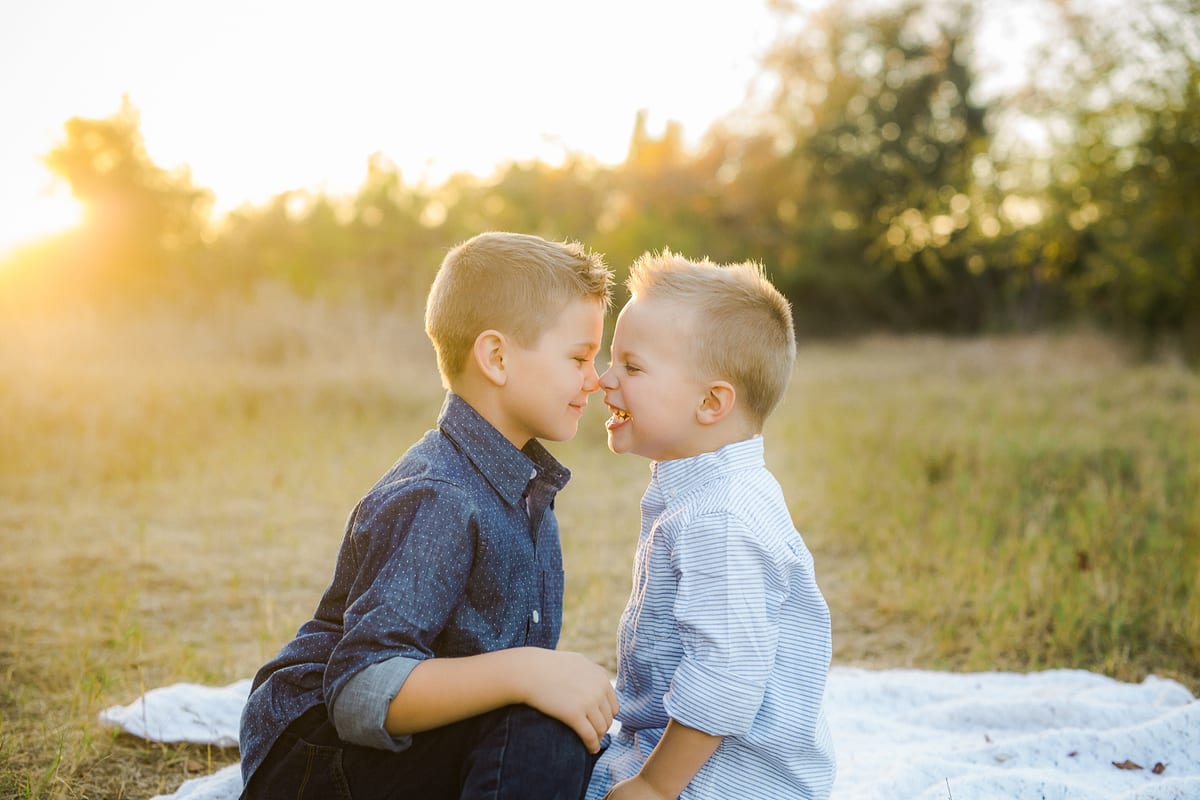 Two brothers touching noses on a blanket in a golden field