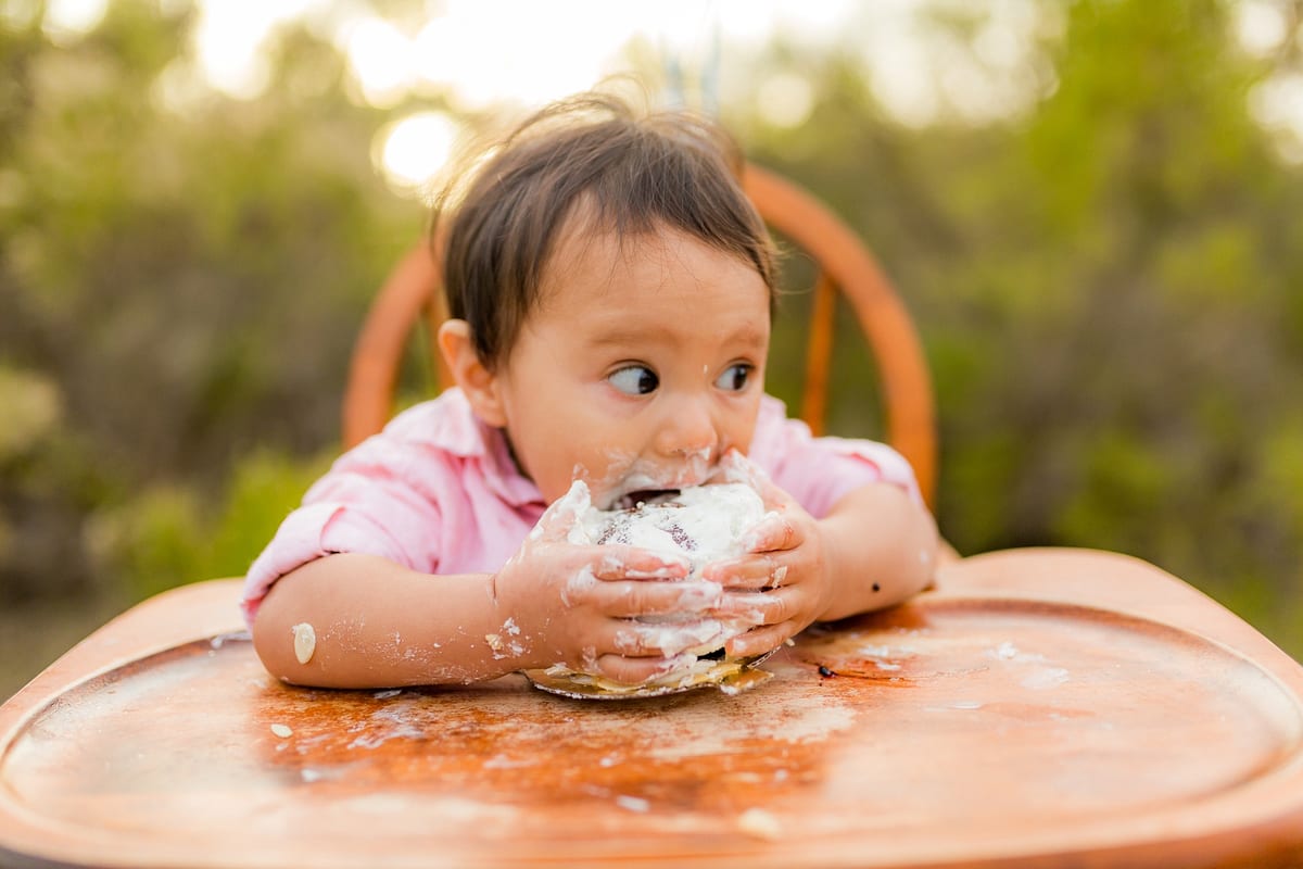 Baby eating her first birthday cake in a wooden high chair