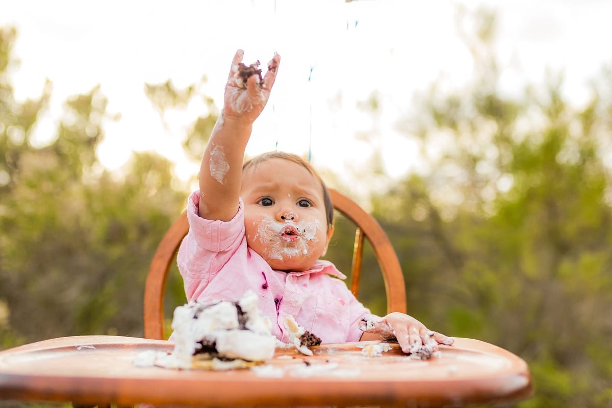 Baby with frosting on her face raising her hand at her cake smash