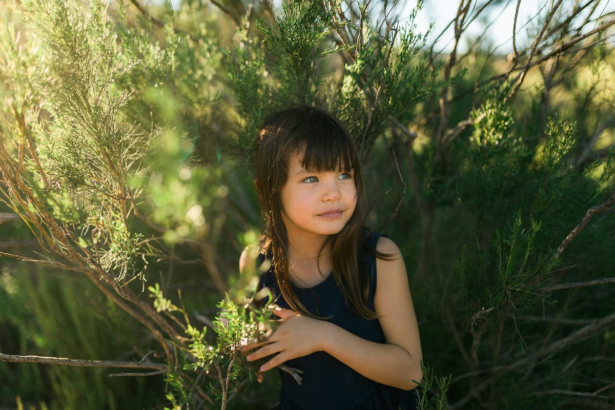 Girl with dark bangs standing among green bushes in soft light