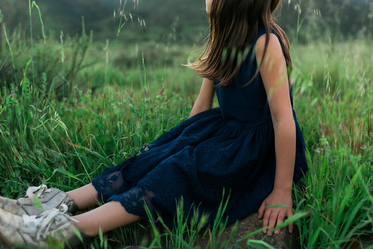Girl in a navy dress sitting in tall grass