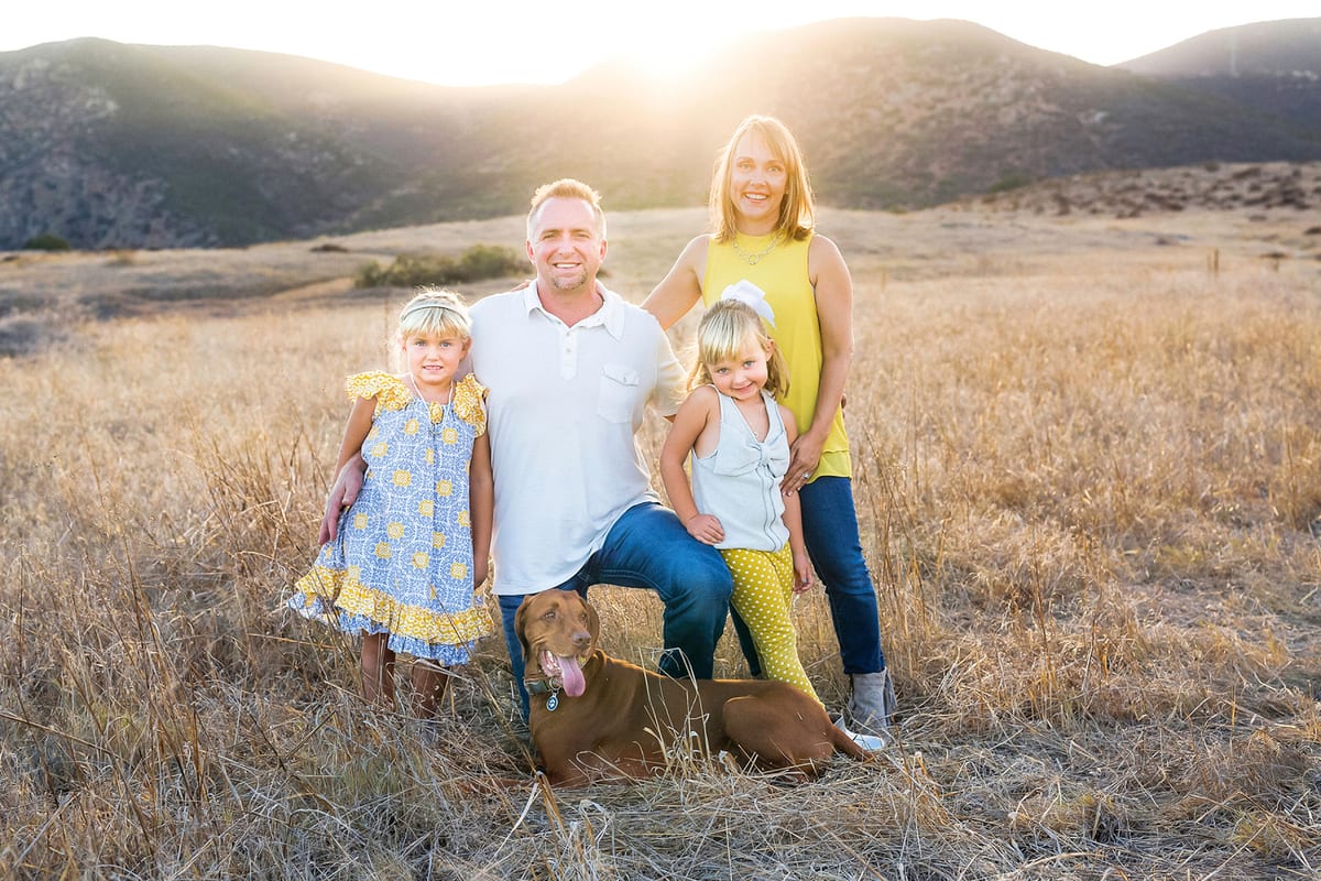 Family of four with their Vizsla in a golden field at sunset