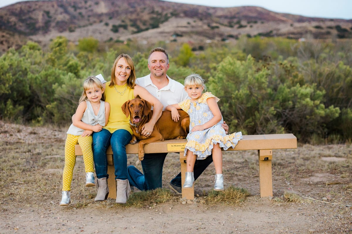 Family of four sitting on a bench with their Vizsla