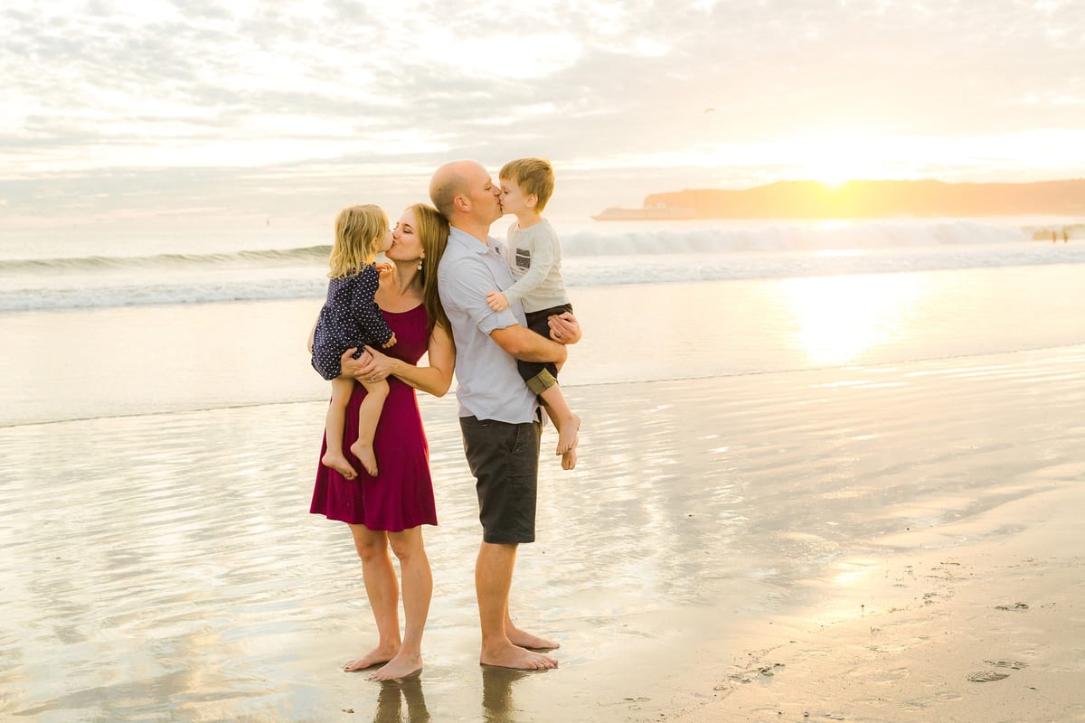 Parents holding and kissing their two children on the beach at sunset