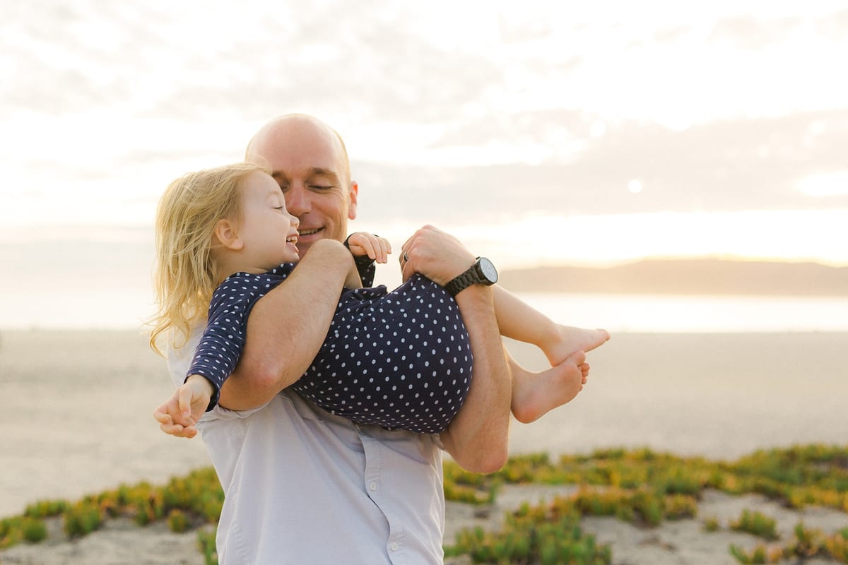 Father swinging his giggling daughter on the beach
