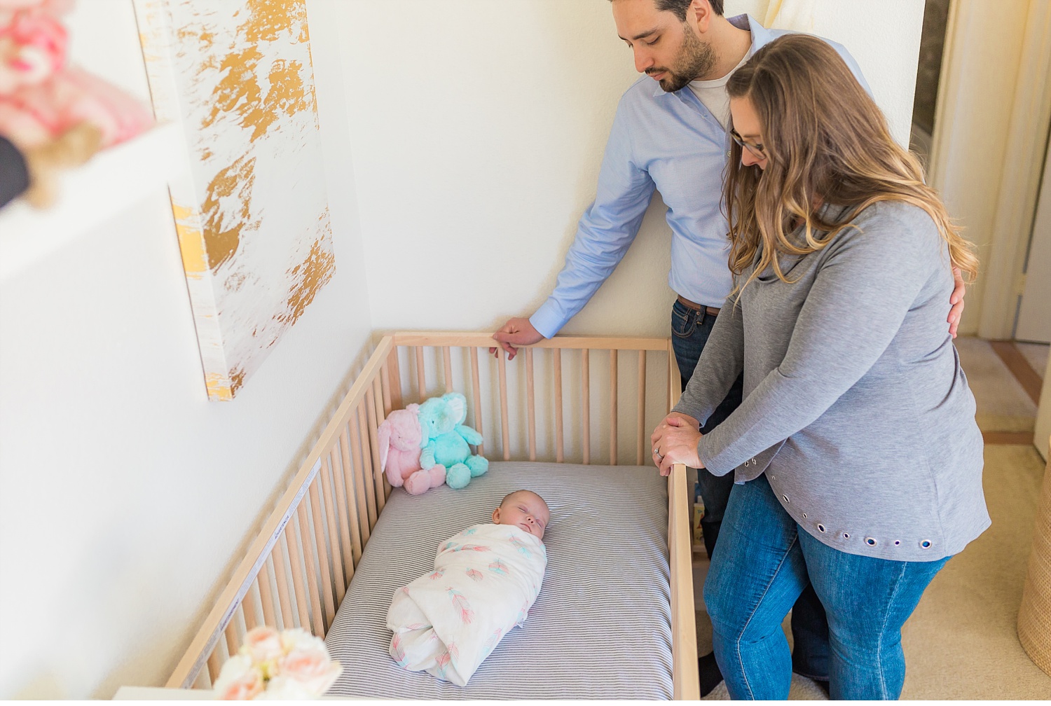Mom and Dad gazing down at their newborn baby in her crib